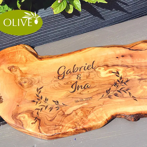 Glattes Schneidebrett aus Olivenholz mit Naturrand und personalisierter Gravur Motiv Reigen mit Namen und Datum in in modernen geschwungenen Schrift. Hier als Frühstücksbrett oder glattes Schneidebrett mit Paarnamen untereinander