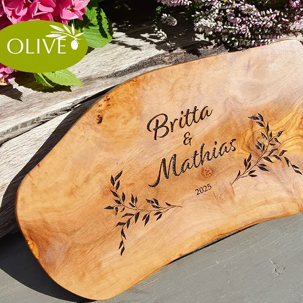 Glattes Schneidebrett aus Olivenholz mit Naturrand und personalisierter Gravur Motiv Reigen mit Namen und Datum in in modernen geschwungenen Schrift. Hier als Frühstücksbrett oder glattes Schneidebrett mit Paarnamen untereinander
