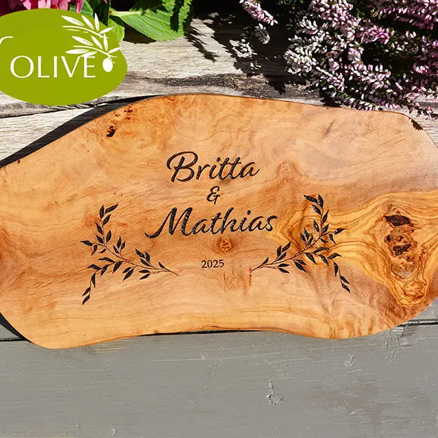 Glattes Schneidebrett aus Olivenholz mit Naturrand und personalisierter Gravur Motiv Reigen mit Namen und Datum in in modernen geschwungenen Schrift. Hier als Frühstücksbrett oder glattes Schneidebrett in verschiedenen Größen und Brettformen