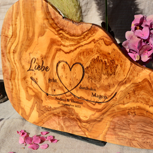 Motiv LIEBE GEHT DURCH DEN MAGEN auf ein Olivenholz glattes Schneidebrett graviert mit personalisierten Namen und Datum und einem geschwungenem Herz