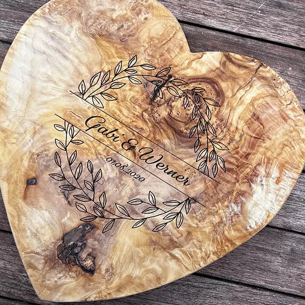 Glattes Schneidebrett aus Olivenholz mit Naturrand und personalisierter Gravur Motiv Blätterkranz mit Namen und Datum in in geschwungener Schrift. Hier als Frühstücksbrett in Herzform oder glattes Schneidebrett in verschiedenen Größen und Brettformen zur Silberhochzeit oder Jubiläum