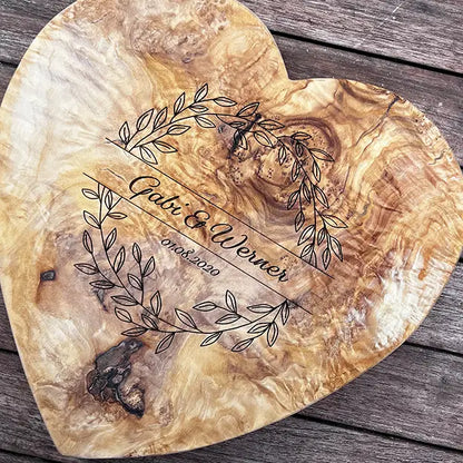 Glattes Schneidebrett aus Olivenholz mit Naturrand und personalisierter Gravur Motiv Blätterkranz mit Namen und Datum in in geschwungener Schrift. Hier als Frühstücksbrett in Herzform oder glattes Schneidebrett in verschiedenen Größen und Brettformen zur Silberhochzeit oder Jubiläum