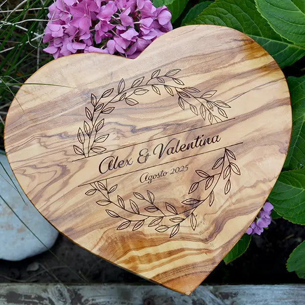 Glattes Schneidebrett aus Olivenholz mit Naturrand und personalisierter Gravur Motiv Blätterkranz mit Namen und Datum in in geschwungener Schrift. Hier als Frühstücksbrett in Herzform oder glattes Schneidebrett in verschiedenen Größen und Brettformen