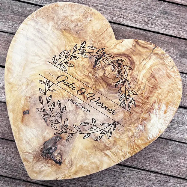 Glattes Schneidebrett aus Olivenholz mit Naturrand und personalisierter Gravur Motiv Blätterkranz mit Namen und Datum in in geschwungener Schrift. Hier als Frühstücksbrett in Herzform oder glattes Schneidebrett in verschiedenen Größen und Brettformen