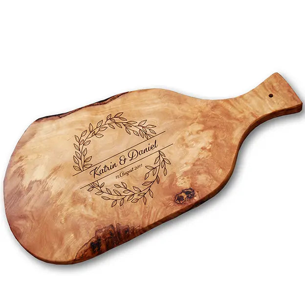 Glattes Schneidebrett aus Olivenholz mit Naturrand und personalisierter Gravur Motiv Blätterkranz mit Namen und Datum in in geschwungener Schrift. Hier als Frühstücksbrett mit Handgriff oder glattes Schneidebrett in verschiedenen Größen und Brettformen