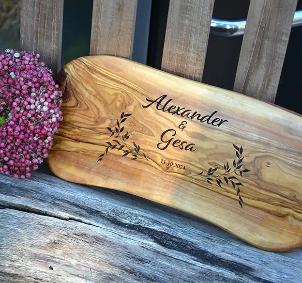 Olivenholz-Frühstücksbrett mit personalisierter Gravur mit dem Motiv Reigen in Form von zwei Blätterzweigen und geschwungener Schrift die Vornamen