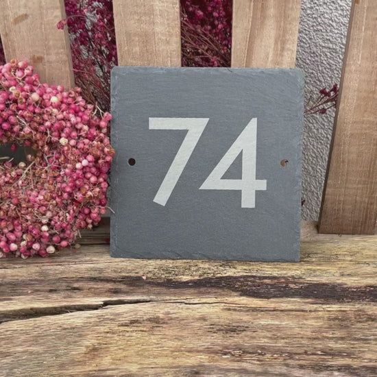 Hausnummer in modernen Ziffern und Buchstaben mit einem Laser auf eine Schieferplatte  in der Größe 15 x 15 cm graviert. Hier Beispiel Nummer 74 mit zwei seitlichen Befestigungslöchern